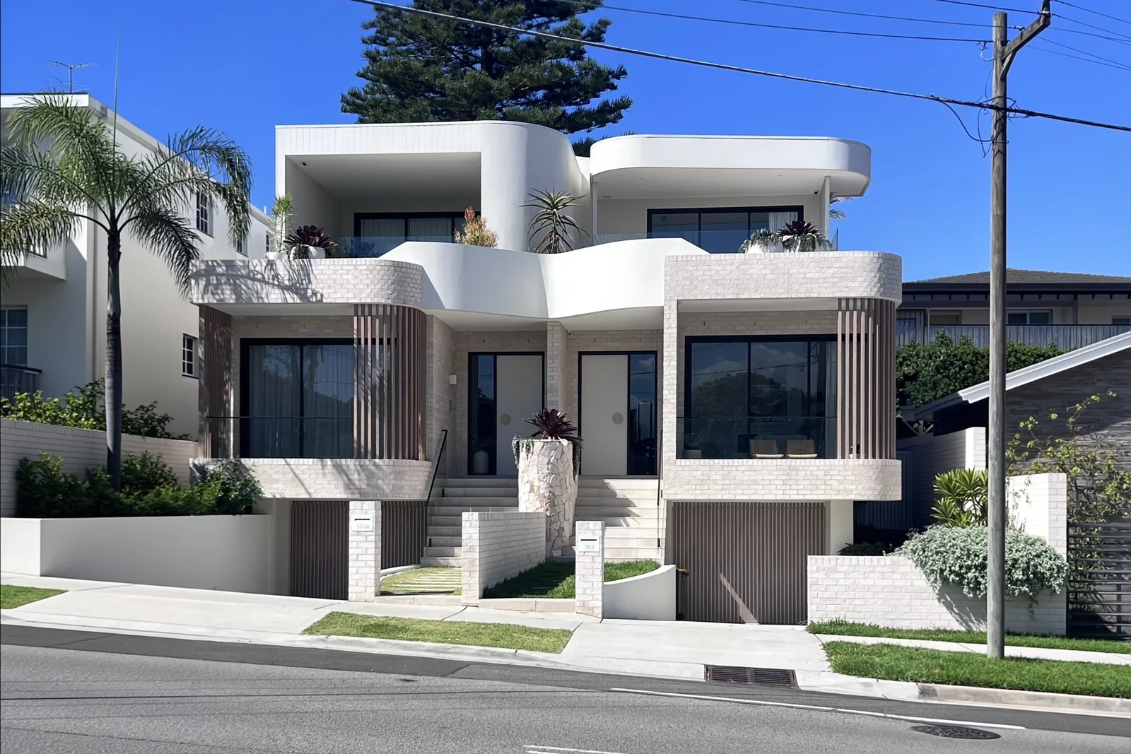Modern two-unit coastal home with brick and curved white architecture.
